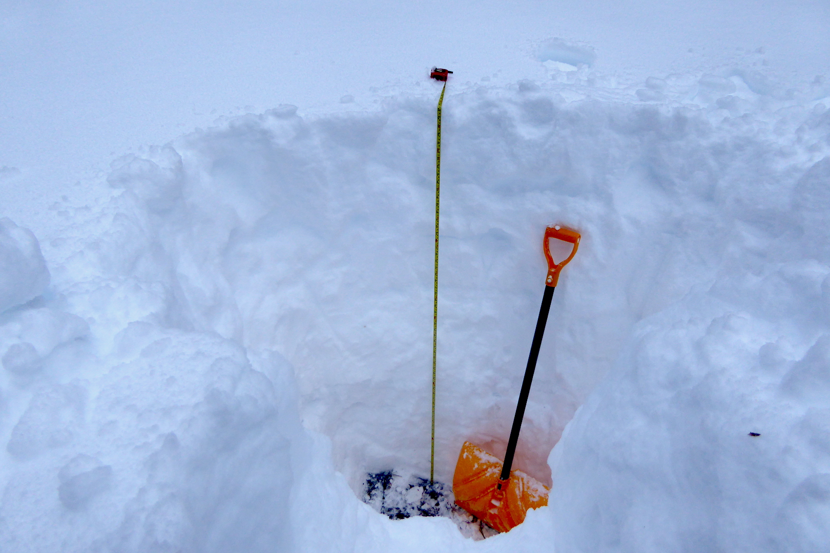 Snow shovel in deep snow next to measuring tape. Tape is 65 inches long.