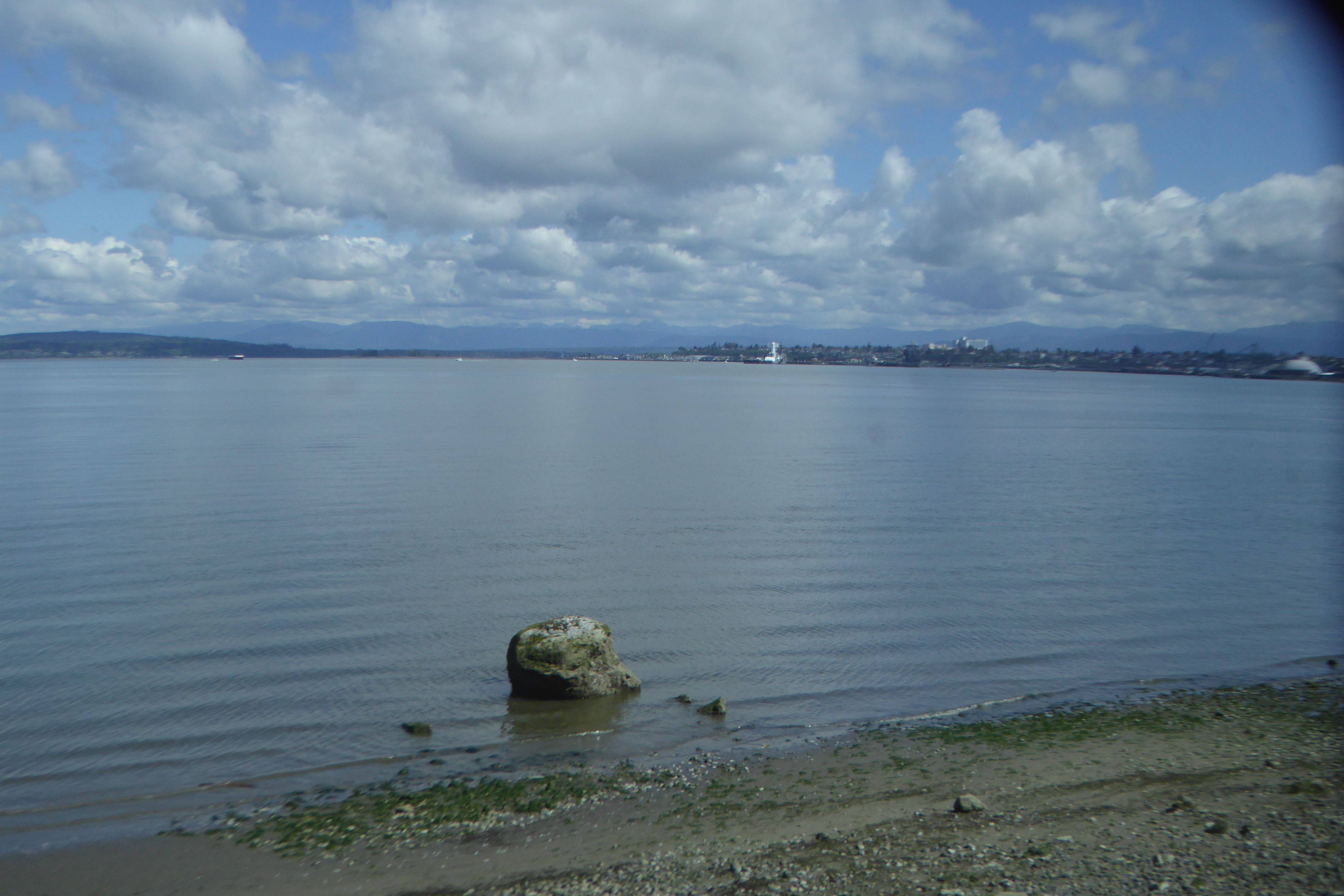 view of water with clouds and boulder in middle foreground