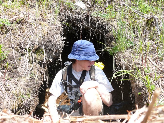 Person squatting in entrance to bear den.