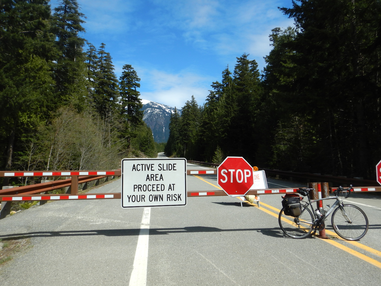 gate across highway. sign reads "Active slide area proceed at your own risk" and "Stop"