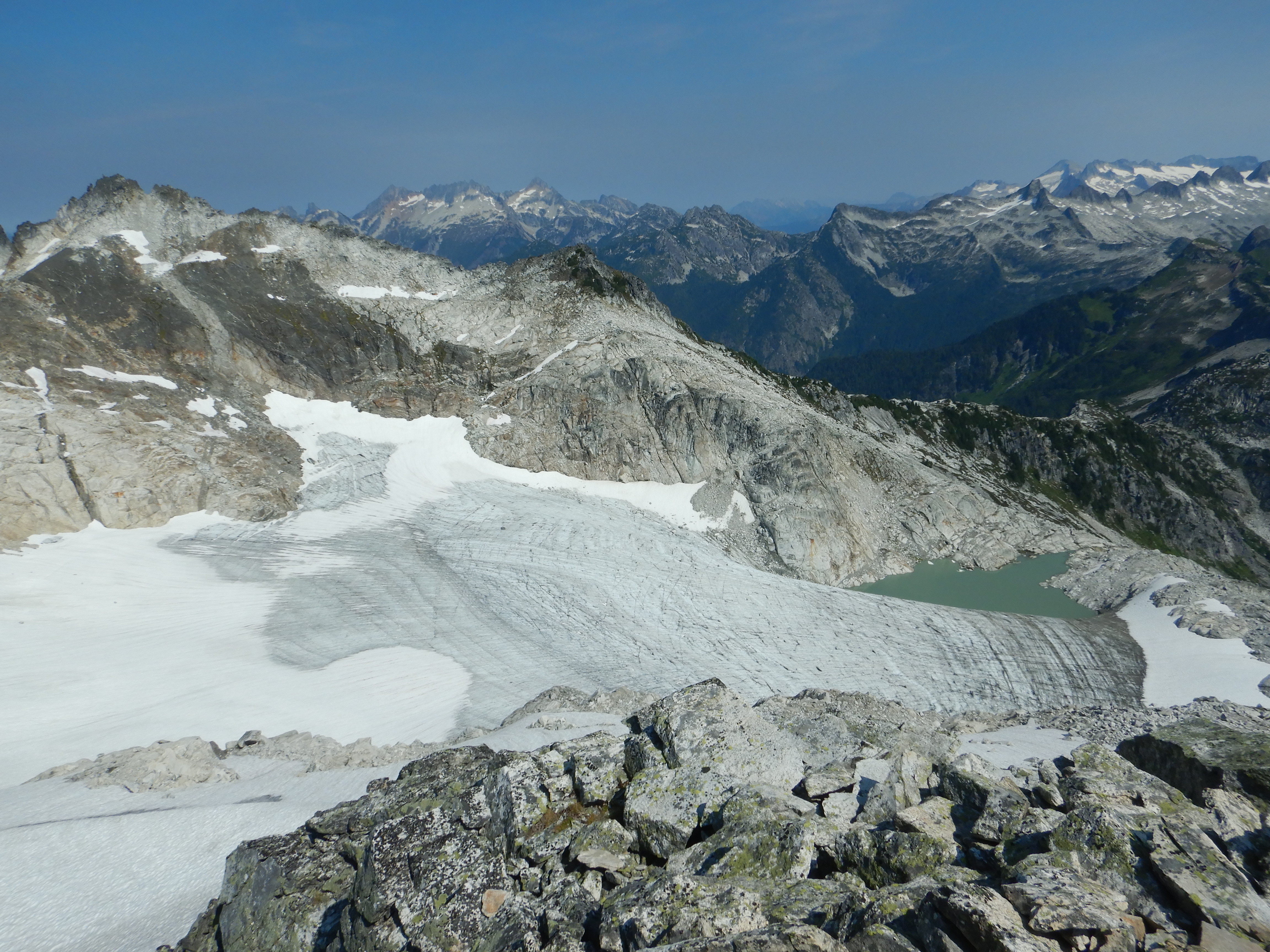 view of glacier in mountain basin. Snow covered mountains on horizon.