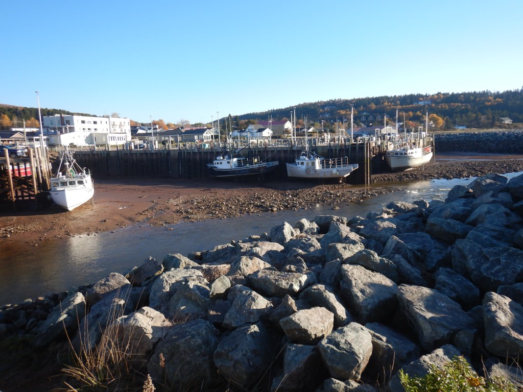 boats rest on exposed land at low tide. A boulder field of riprap fills the foreground while a small river flows in between.
